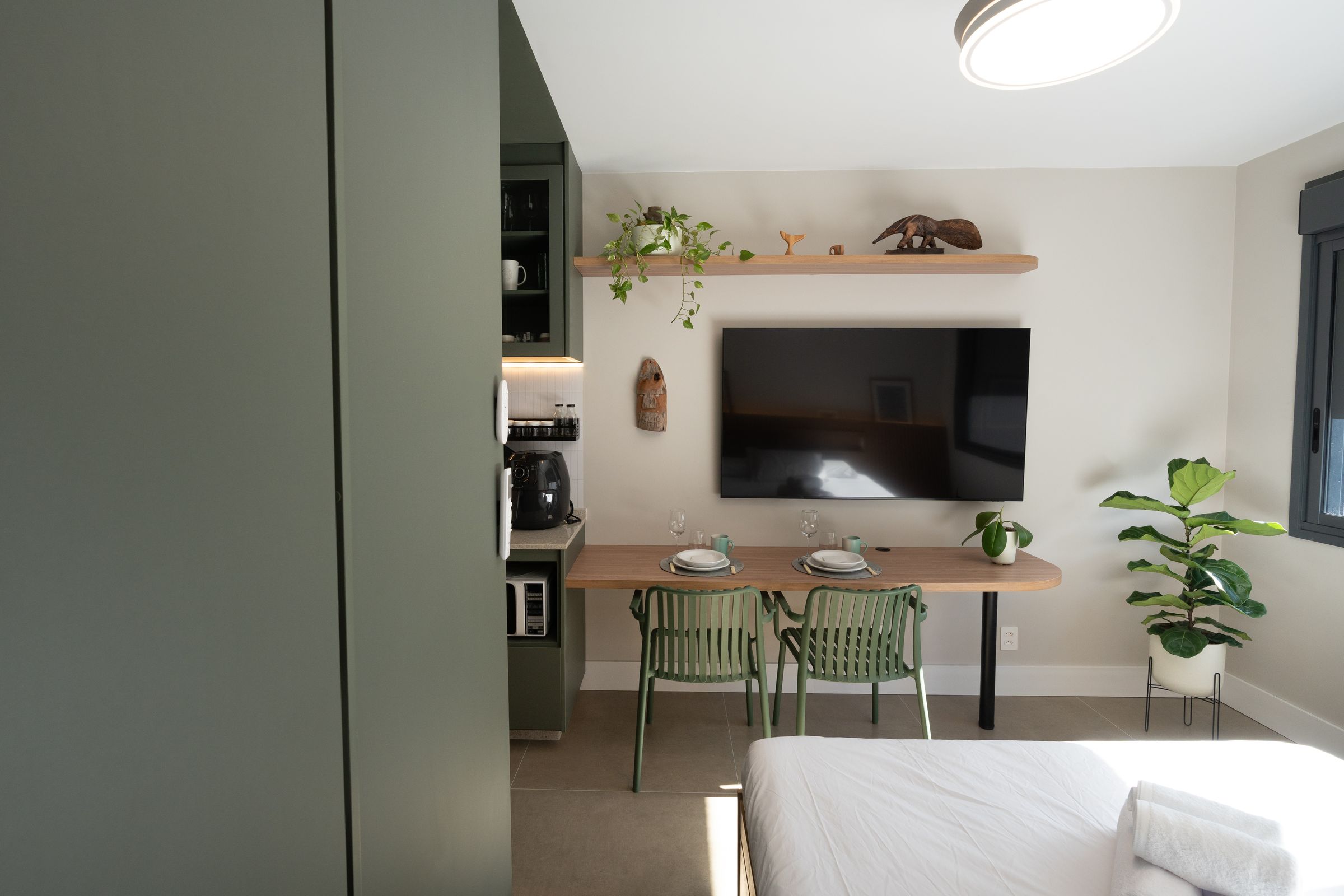 Studio 215 visto da cama, com mesa de jantar, Smart TV e cozinha ao fundo